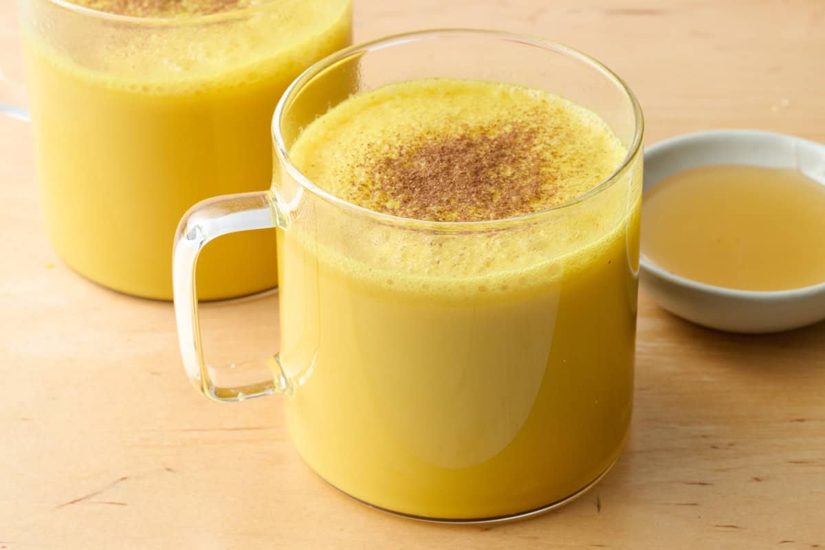 the best ginger turmeric Golden Milk latte in a glass mug with a small dish of honey nearby.