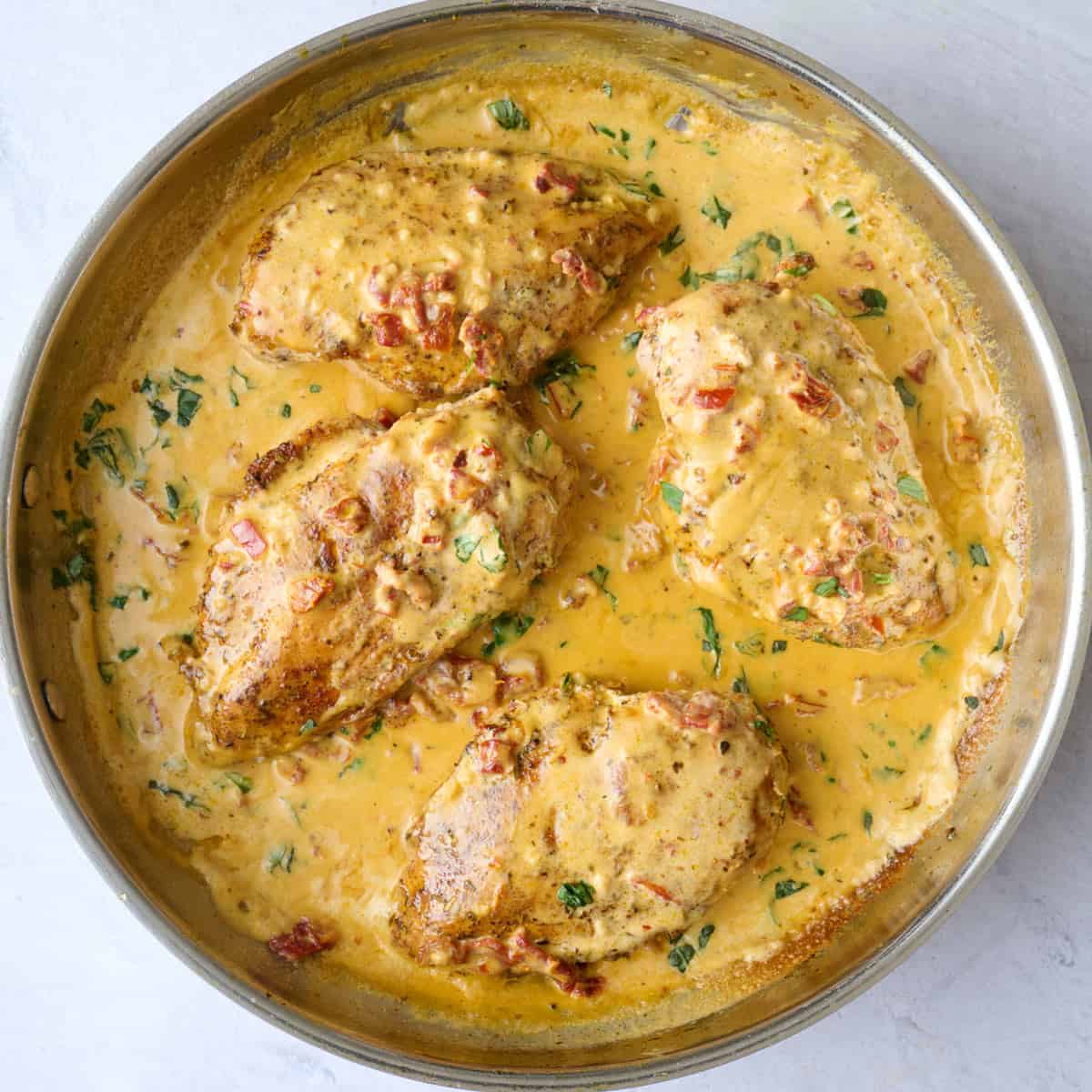 Creamy sun dried tomato sauce in a skillet with cooked chicken breasts tossed in sauce.