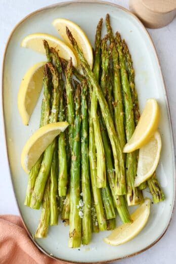 Easy roasted asparagus on a platter with lemon wedges.
