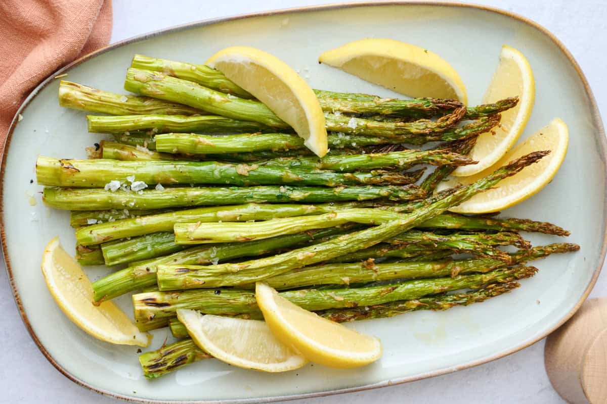 Best oven roasted asparagus recipe on a platter with lemon wedges.