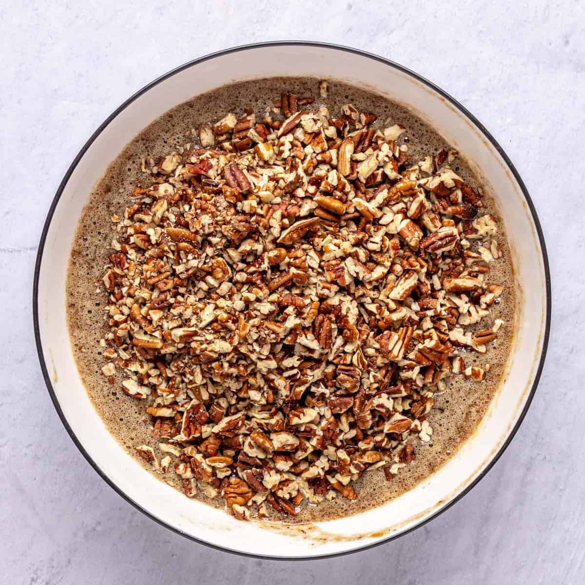 Date mixture in a bowl with chopped pecans added on top before mixing.