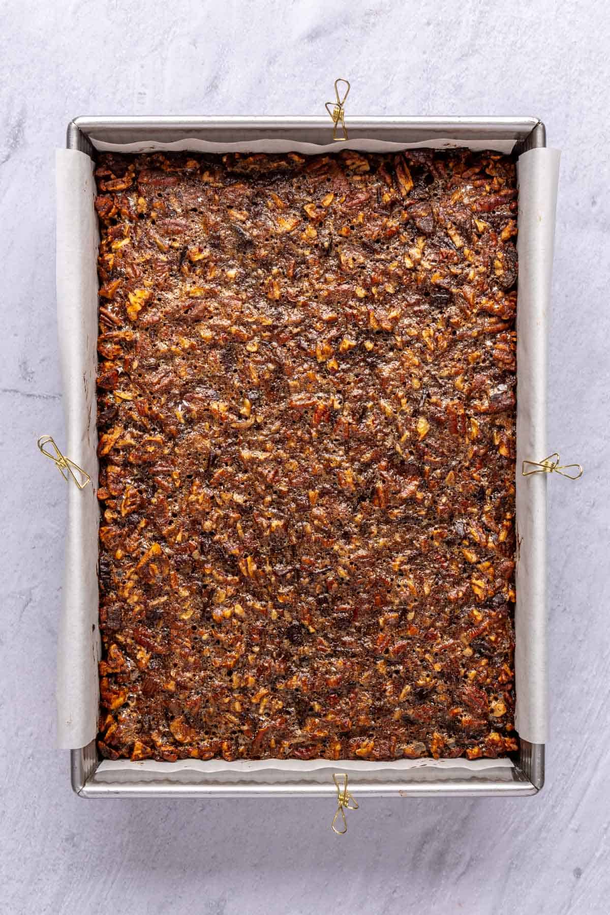 Pecan bars after baking in a parchment lined baking dish.