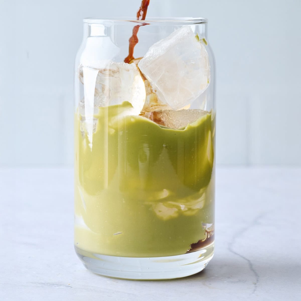 Espresso being poured into a glass with ice and pistachio cream.