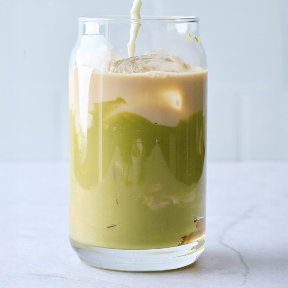 Cream being poured into a glass with pistachio butter, ice and espresso.