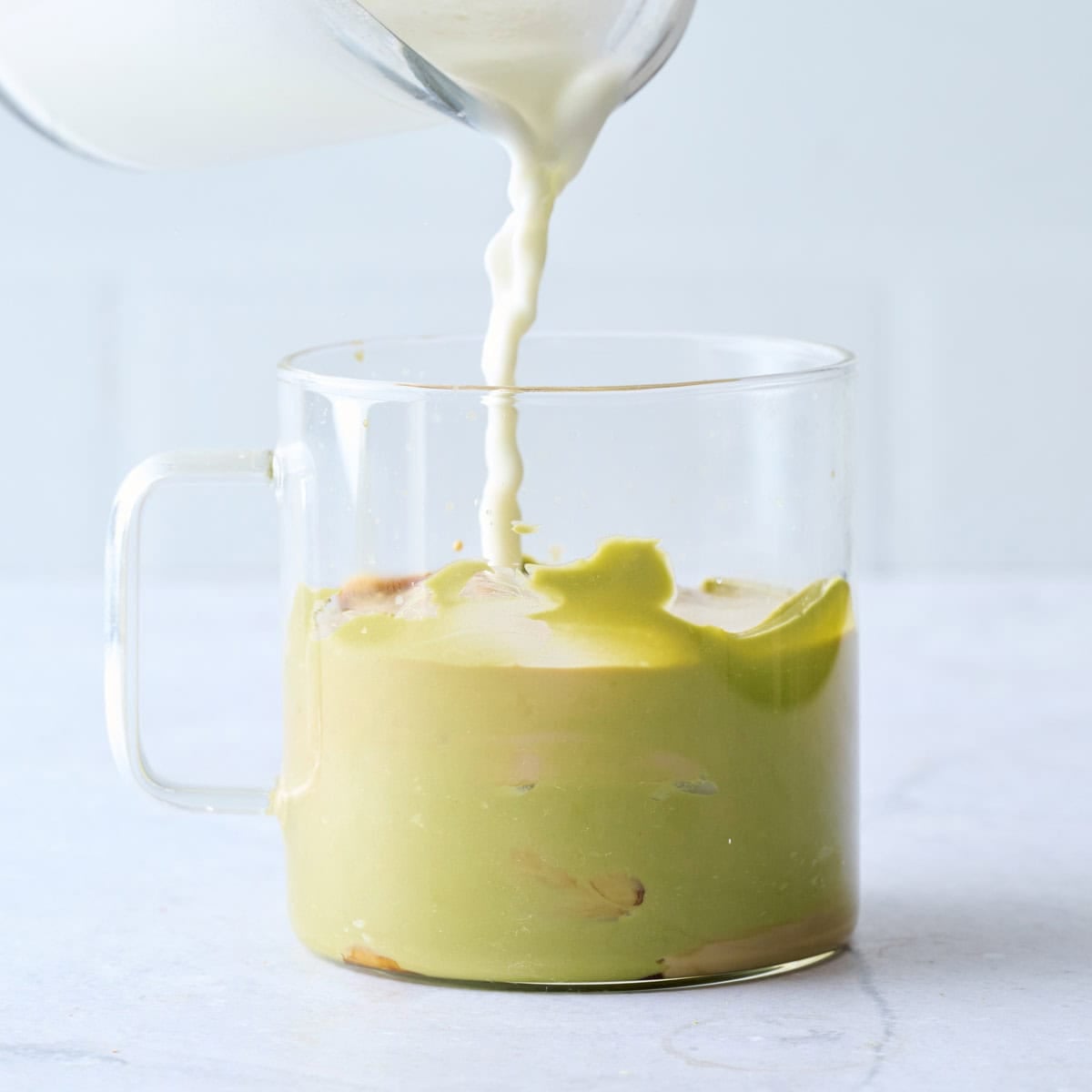 Milk being poured into a glass mug with espresso and pistachio cream.