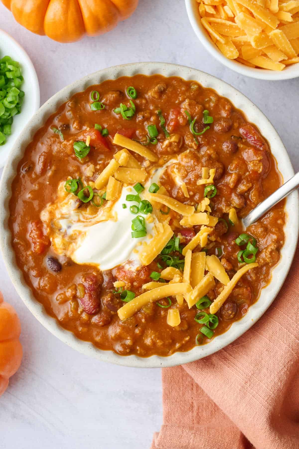 Pumpkin puree chili recipe served in a bowl and topped with sour cream, shredded cheddar cheese and green onions.