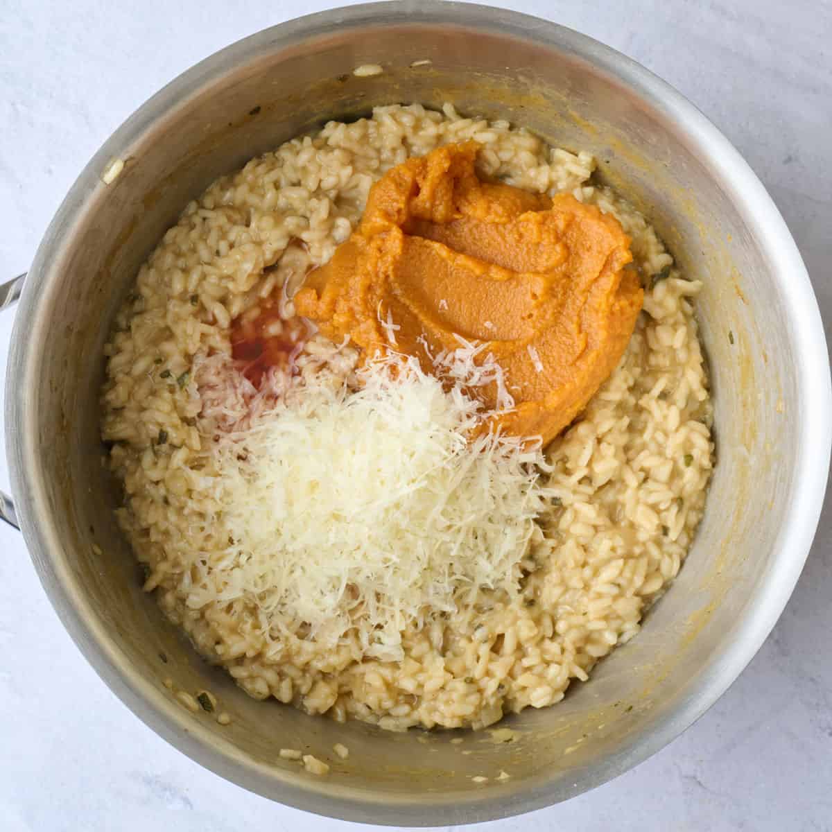 Pumpkin puree and parmesan cheese added on top of risotto in a pot before combining.