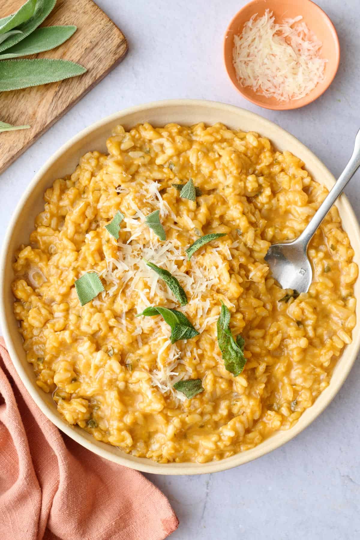 Creamy no stir pumpkin risotto in a serving bowl garnished with parmesan cheese and fried sage leaves.