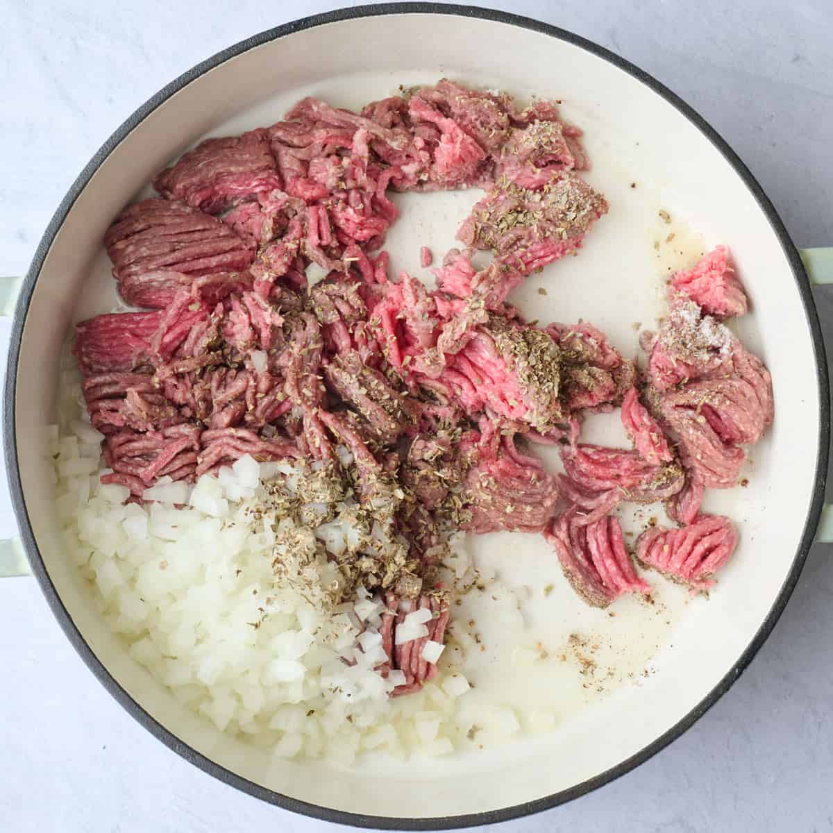 Lean ground beef broken into large chunks with diced onions and seasonings before combining.