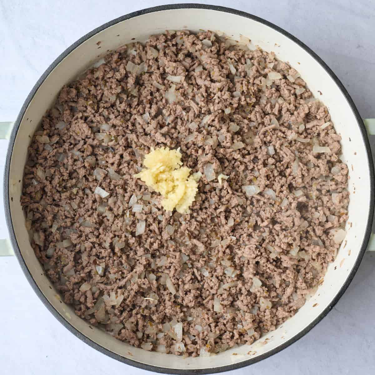 Garlic added to a pot of cooked ground beef and onions before combining.