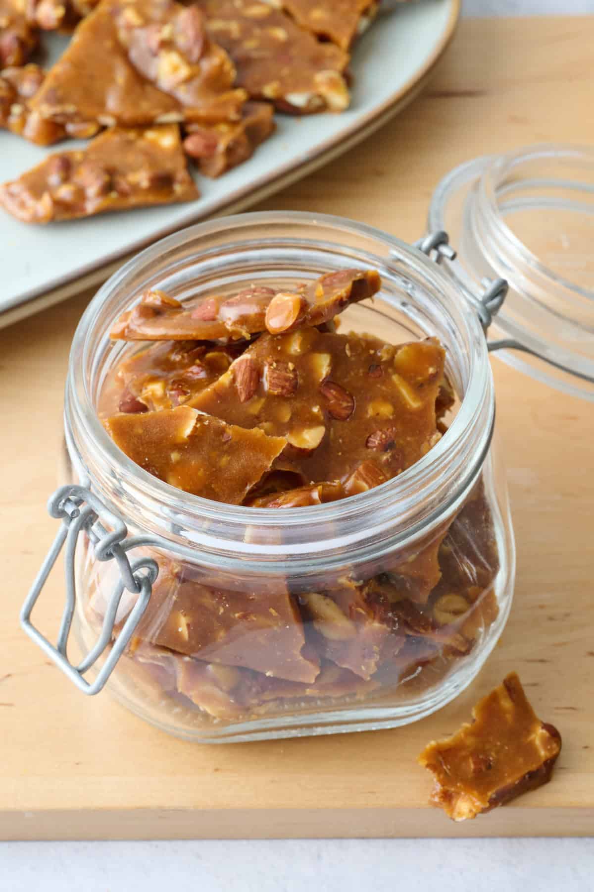 Homemade almond brittle recipe with pieces stored in a small glass jar.