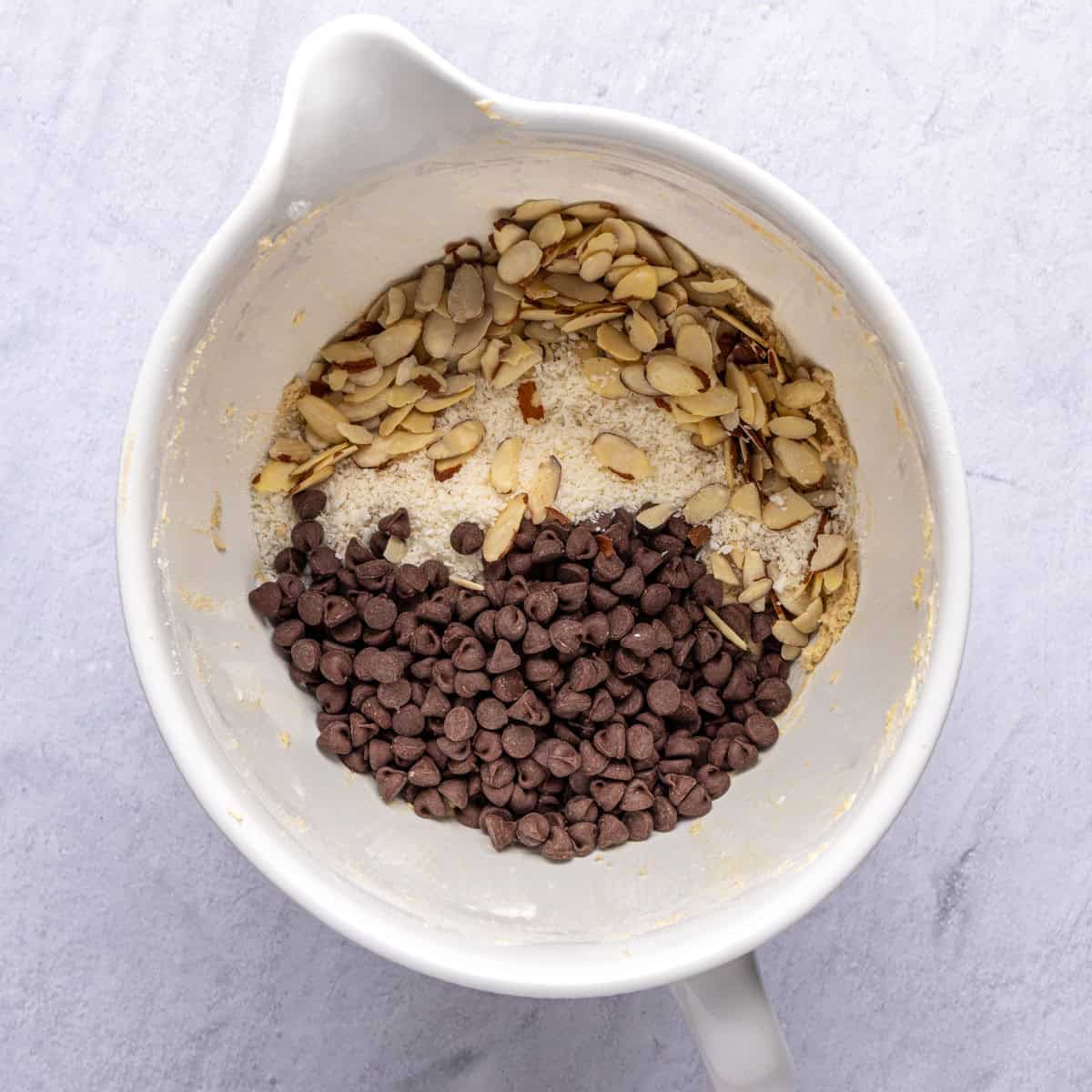 Chocolate chips, shredded coconut, and sliced almonds added on top of cookie dough in mixing bowl before combining.