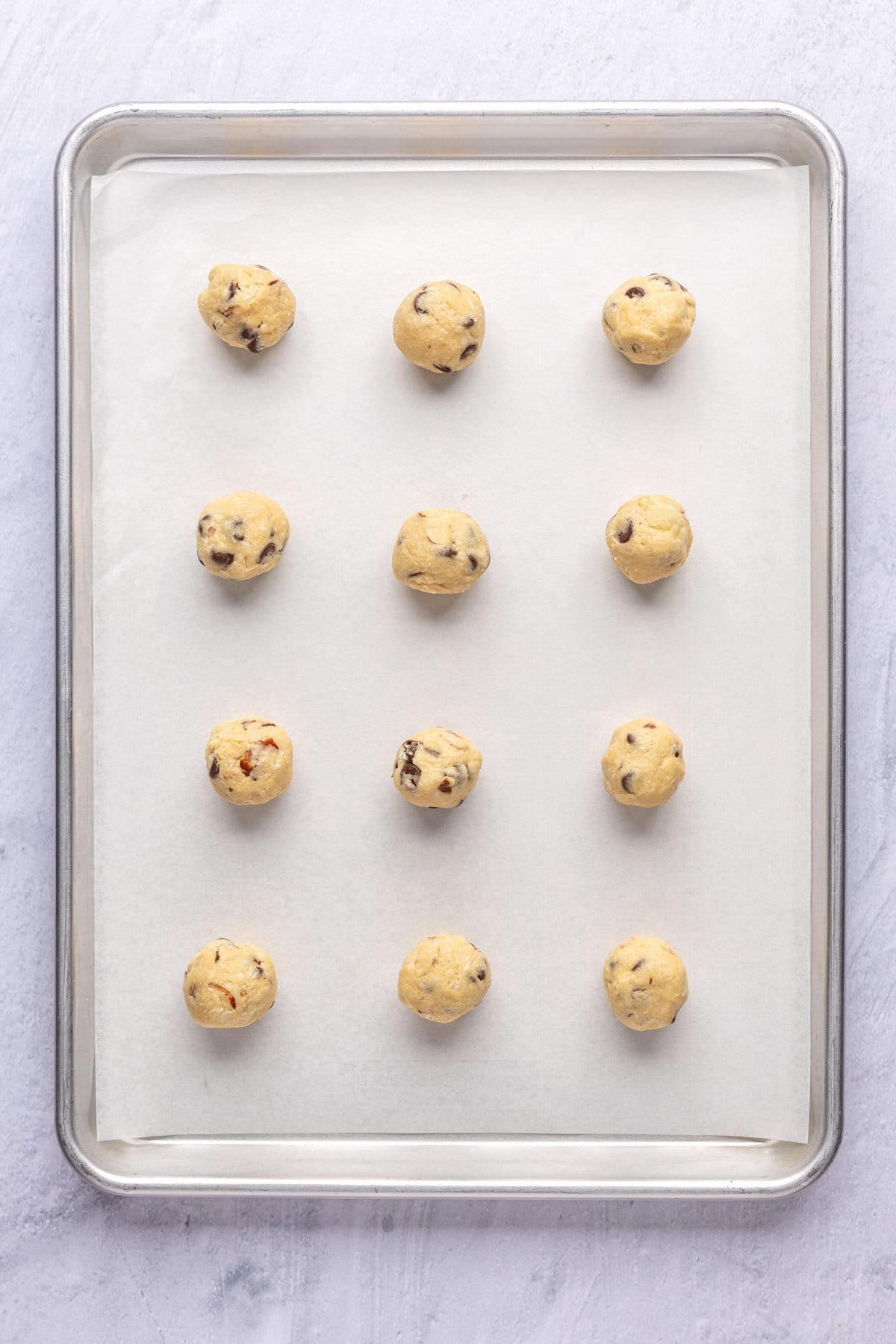 Coconut almond cookie dough balls on a parchment lined baking sheet before baking.