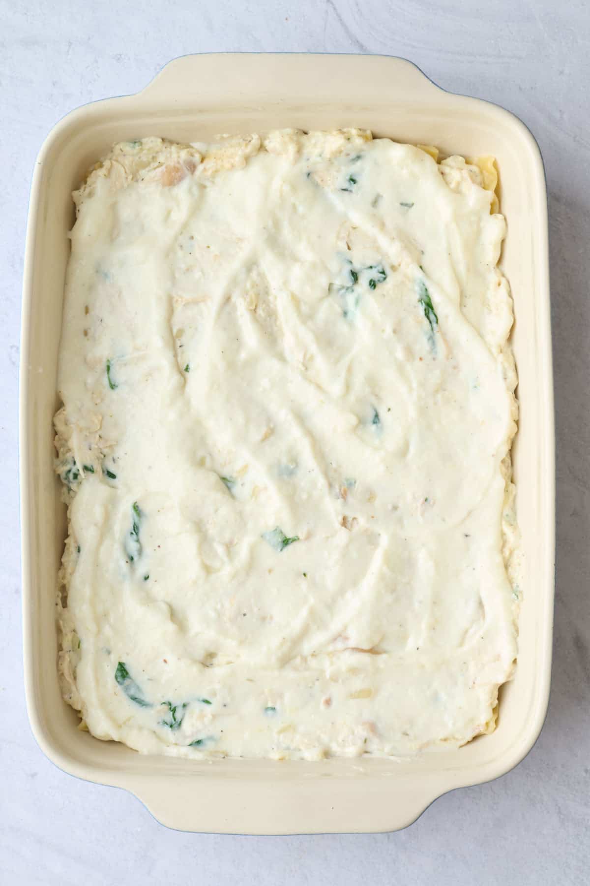 Par cooked lasagna pasta sheets layered on top of sauce with chicken ricotta mixture added on top.