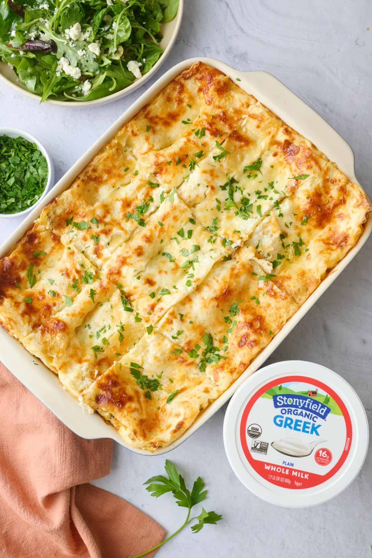 Chicken lasagna made with Stonyfield Whole Milk Greek Yogurt in a baking dish cut into 9 servings and garnished with chopped parsley.