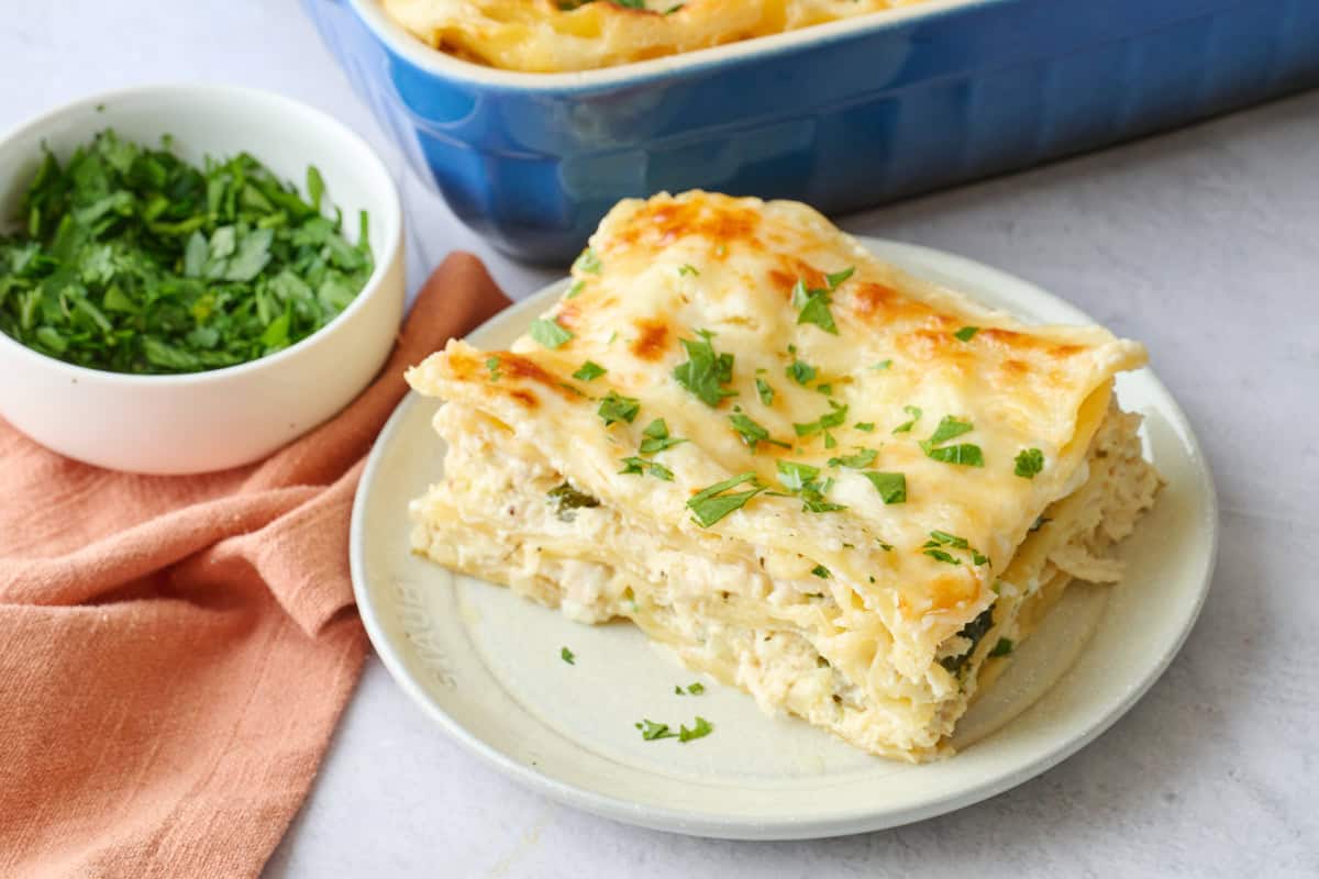 Serving of white chicken lasagna on a small plate with baking dish nearby.
