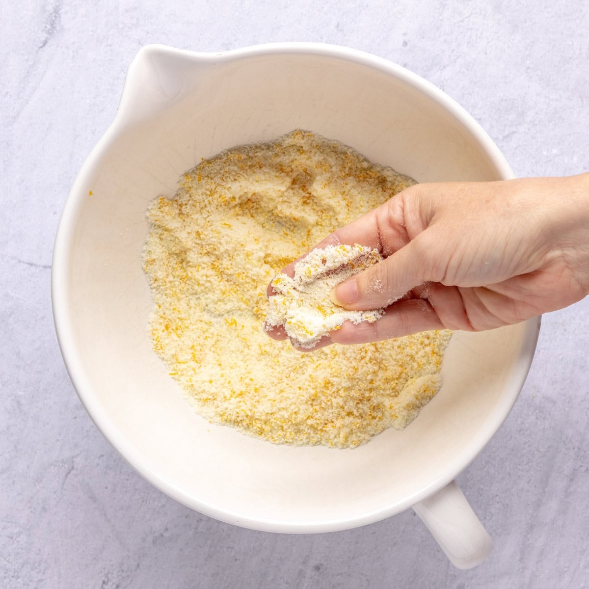Fingers rubbing sugar and orange zest together in a bowl.