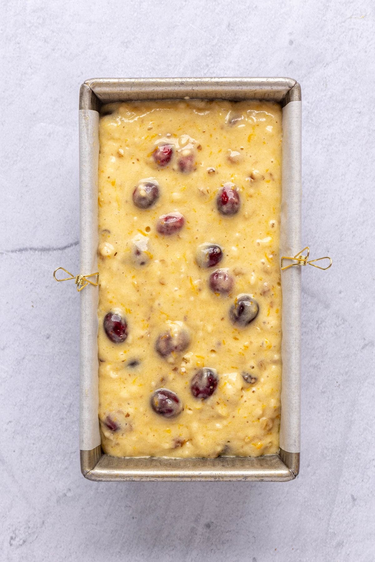 Cranberry orange bread batter in a parchment lined loaf pan before baking.