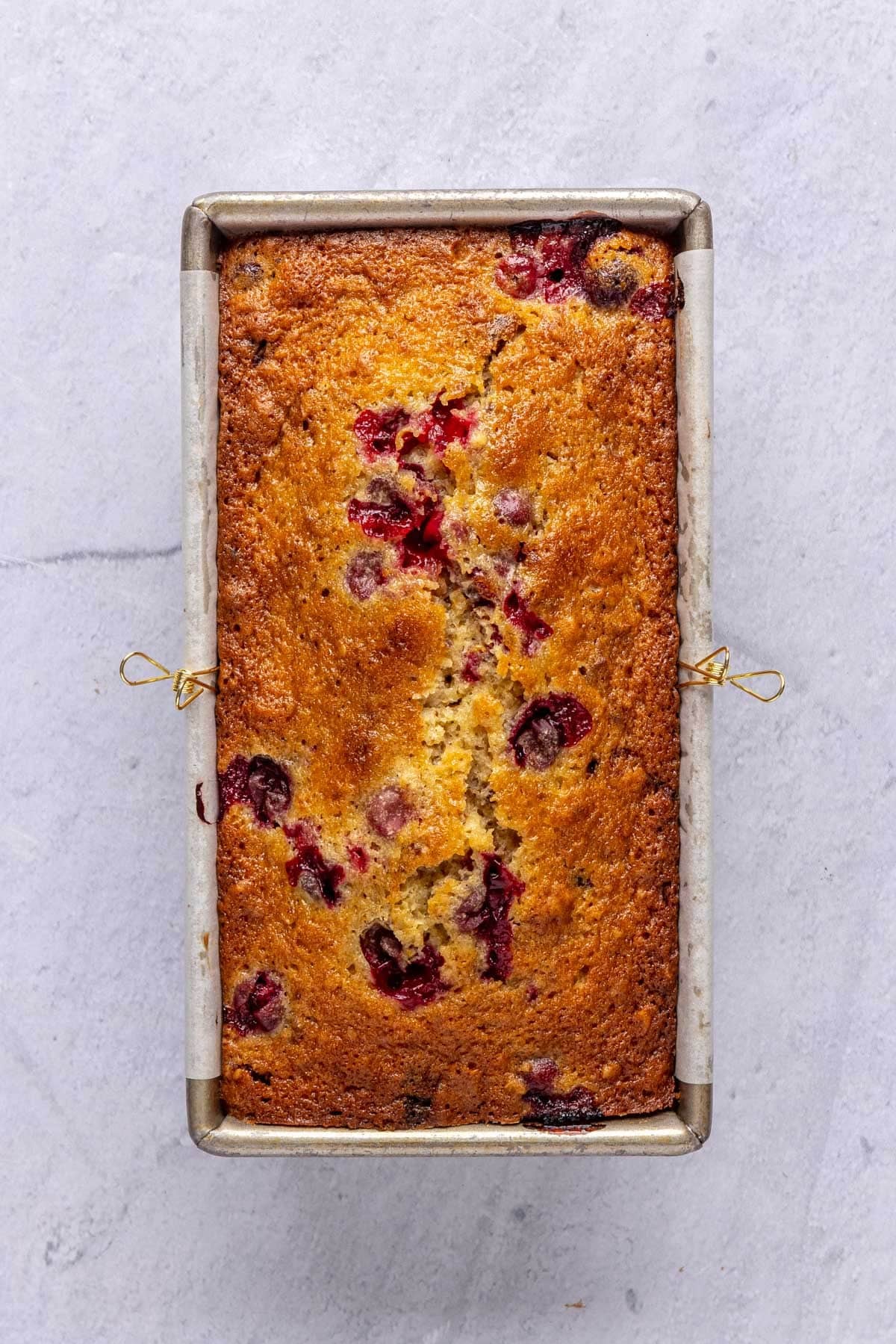 Bread recipe after baking with bursted cranberry juice peeking through the top of the loaf.