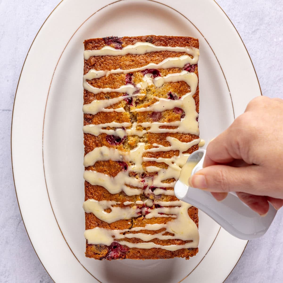Homemade orange glaze being poured over cranberry bread.