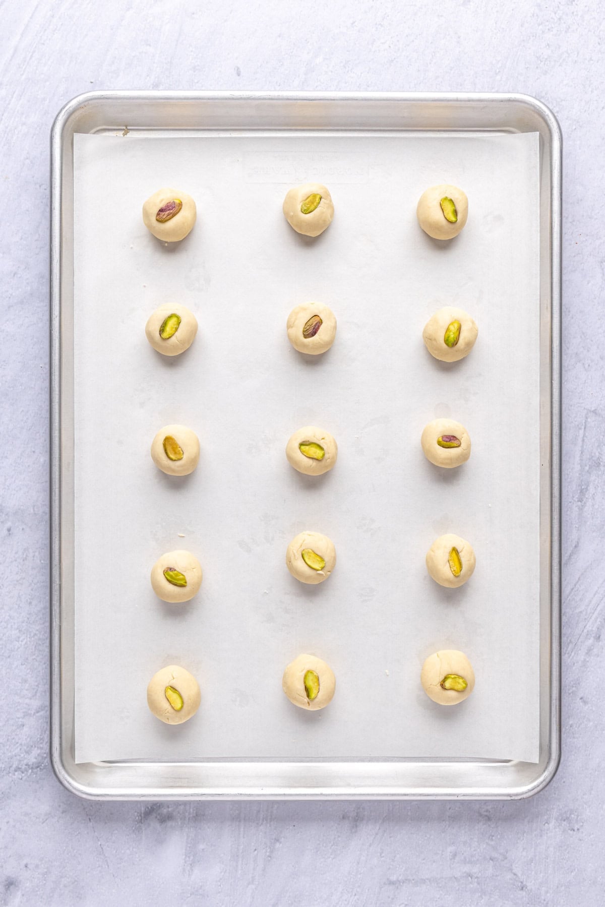 Buttery Middle Eastern shortbread cookie dough balls on a parchment lined baking sheet with a pistachio pressed on top of each one before baking.