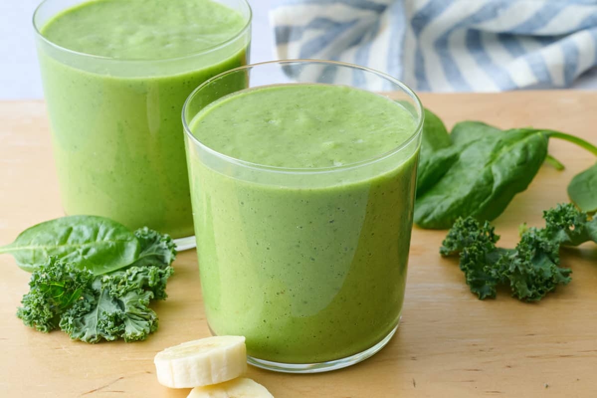 Green breakfast smoothie recipe in two glasses, made with spinach, kale, avocado, pineapple and banana.