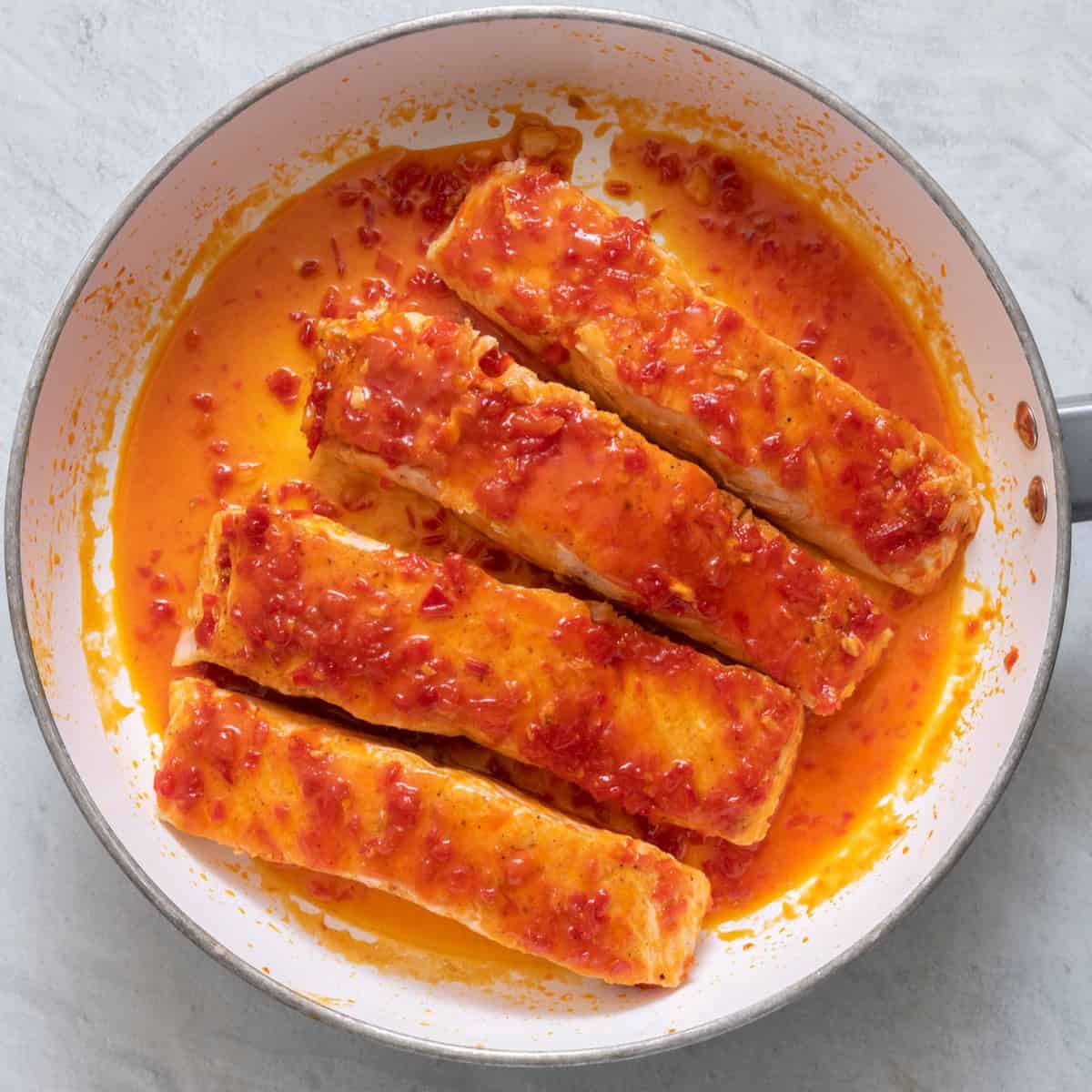 Salmon filets in a pan after being glazed with a sweet and spicy harissa sauce.