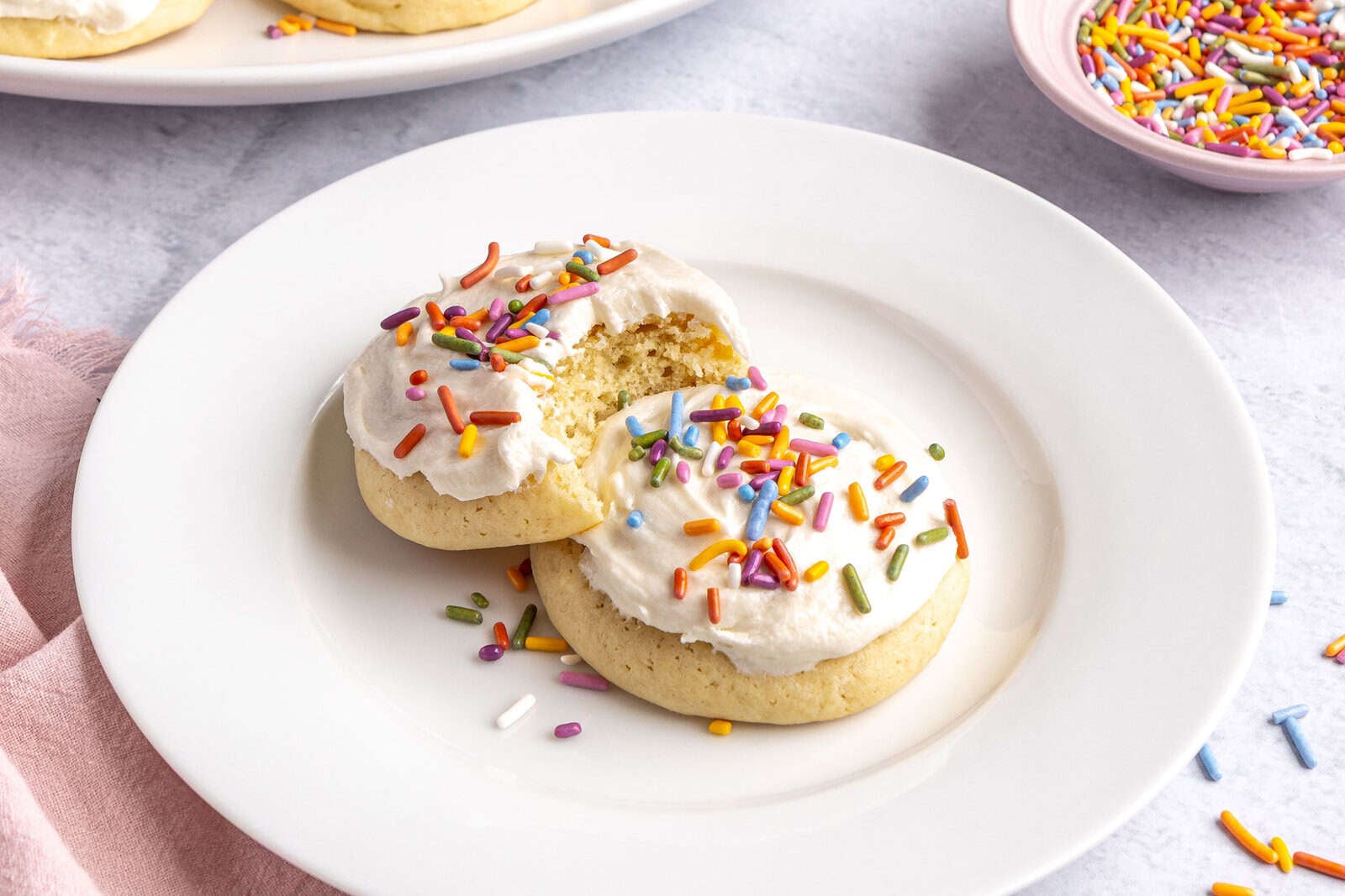 Soft Lofthouse frosted sugar cookies on a plate with buttercream frosting and sprinkles on top/
