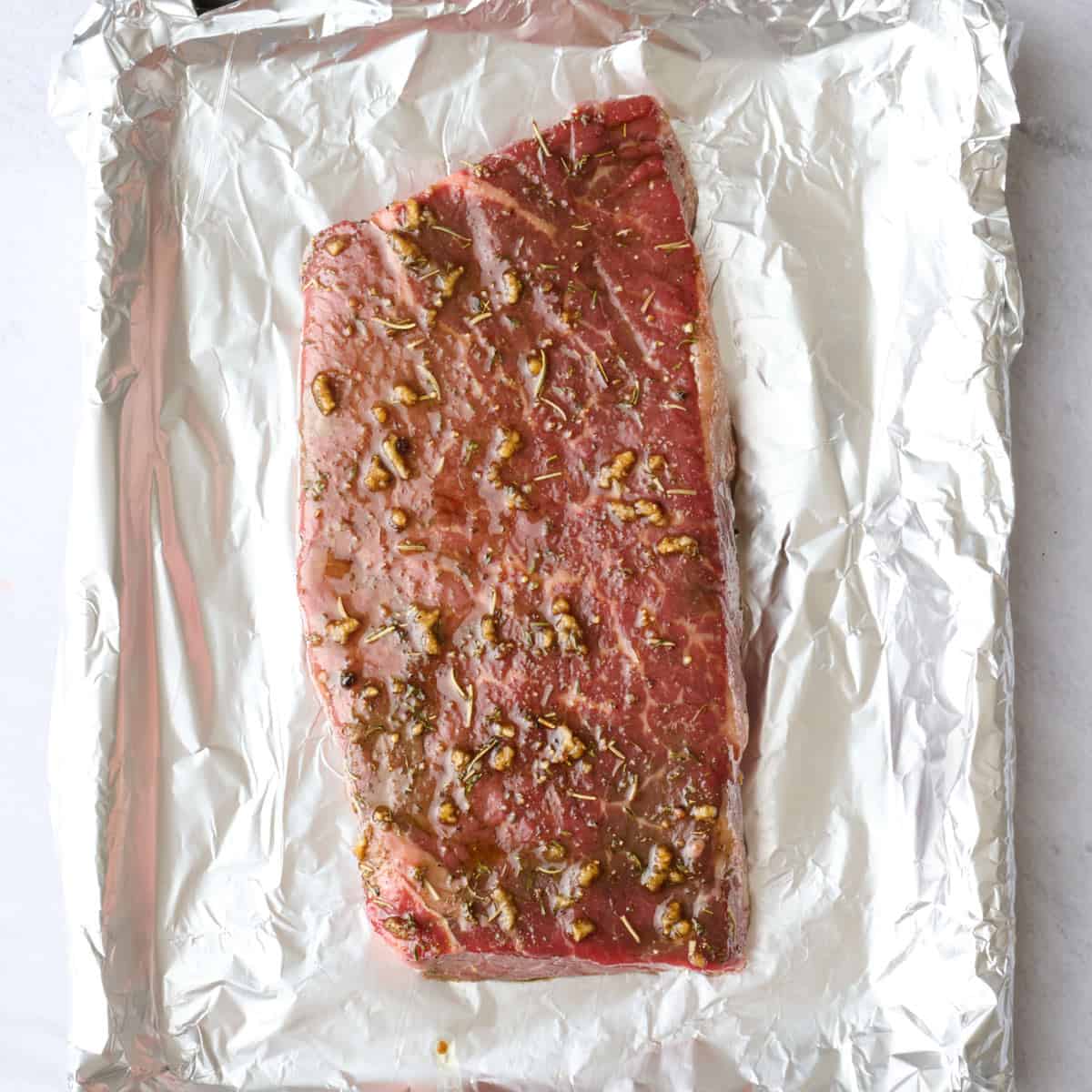 Foiled lined sheet pan with marinated meat on top after extra marinade drips off before broiling.