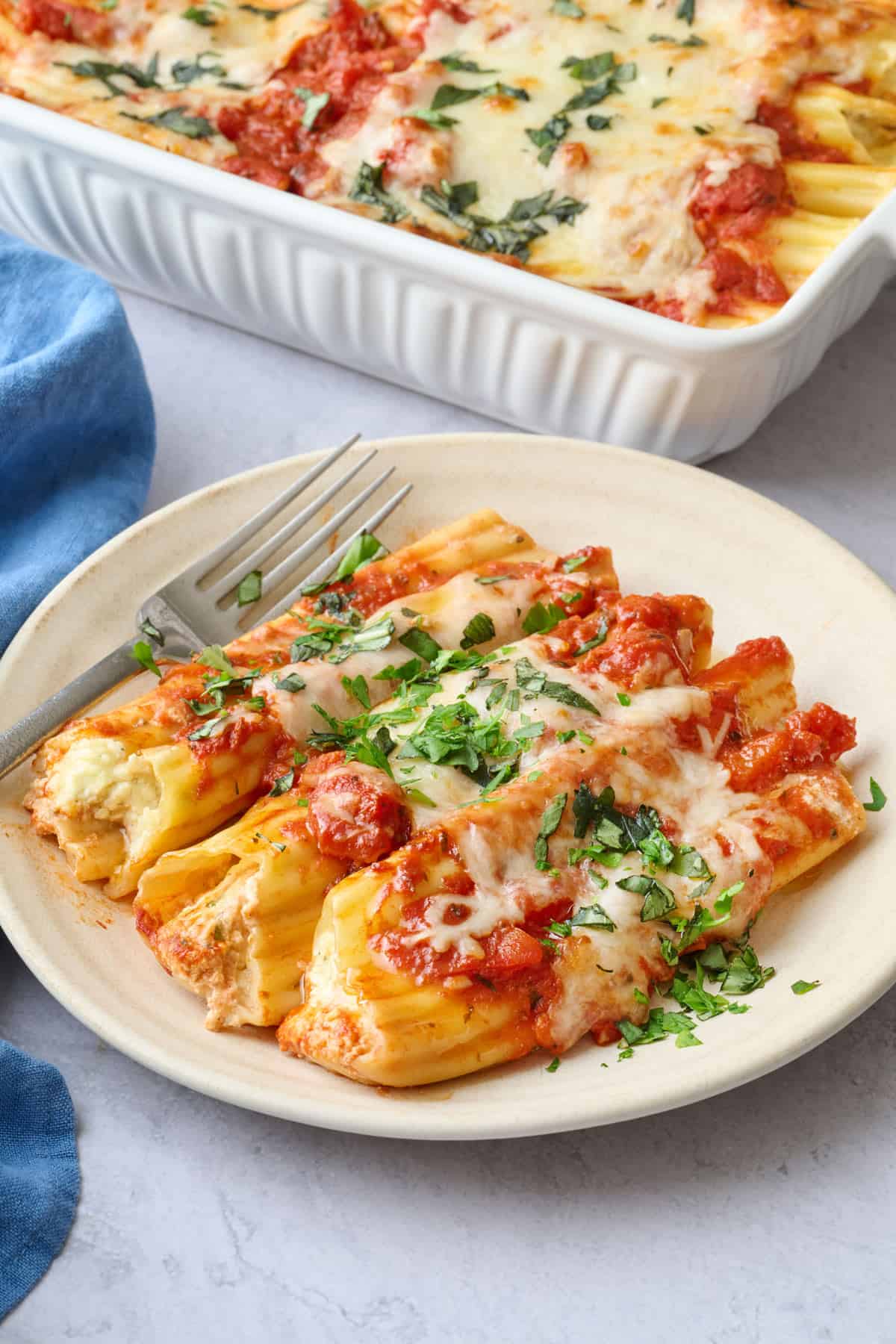 Best manicotti recipe served on a small plate with baking dish nearby.