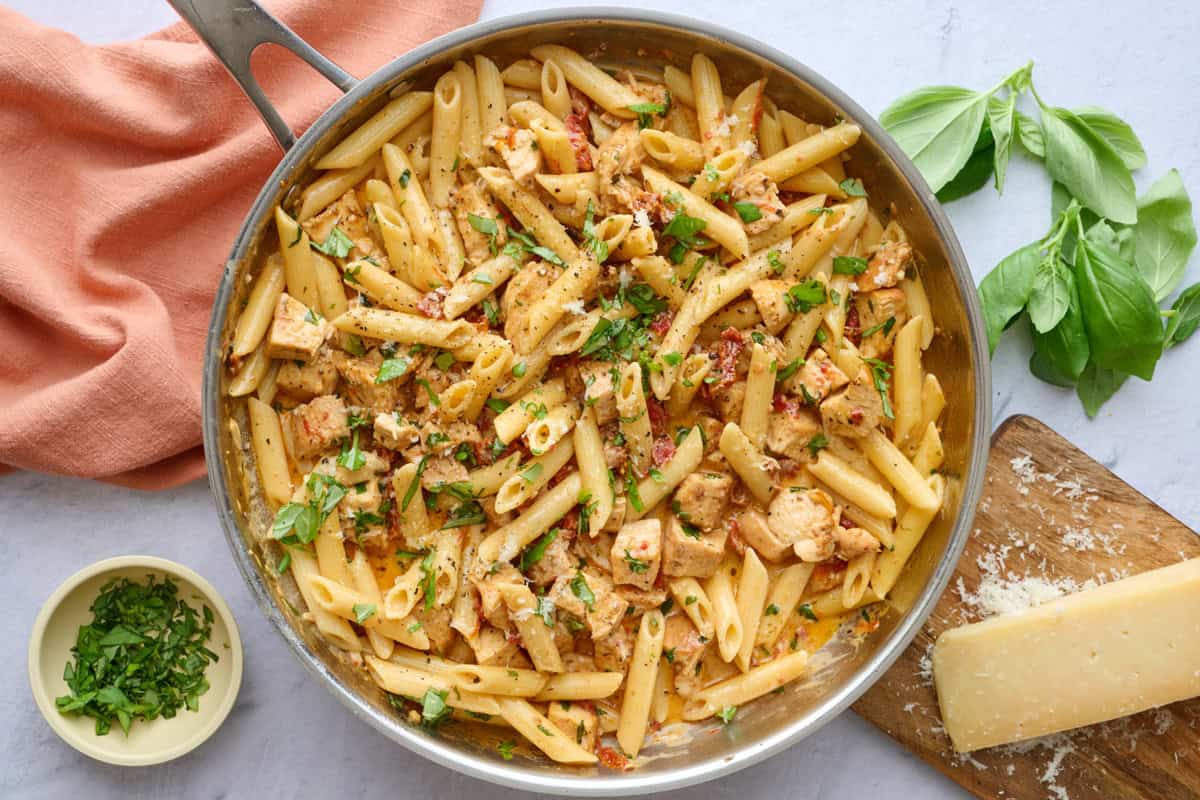 Viral TikTok Marry me pasta with chicken in a skillet with a wooden serving spoon dipped inside, garnished with extra chopped basil and grated parmesan.
