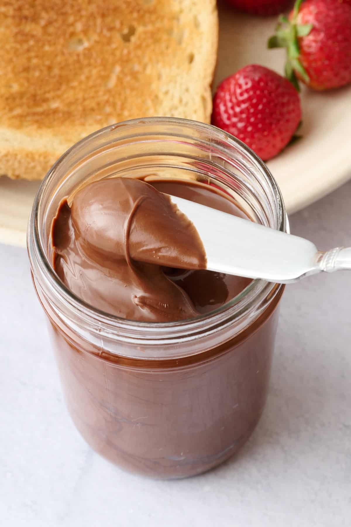 Knife lifting up some smooth and creamy homemade nutella from a glass jar.