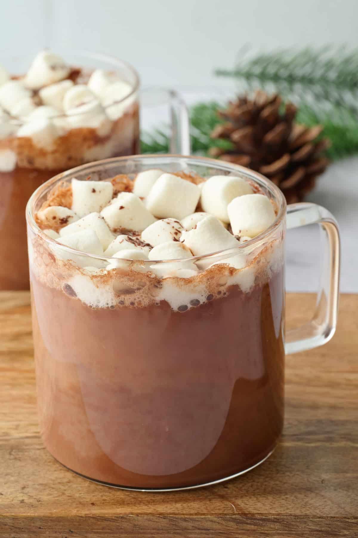 Two glass mugs of vegan hot chocolate made with almond milk and topped with mini marshmallows and chocolate shavings,