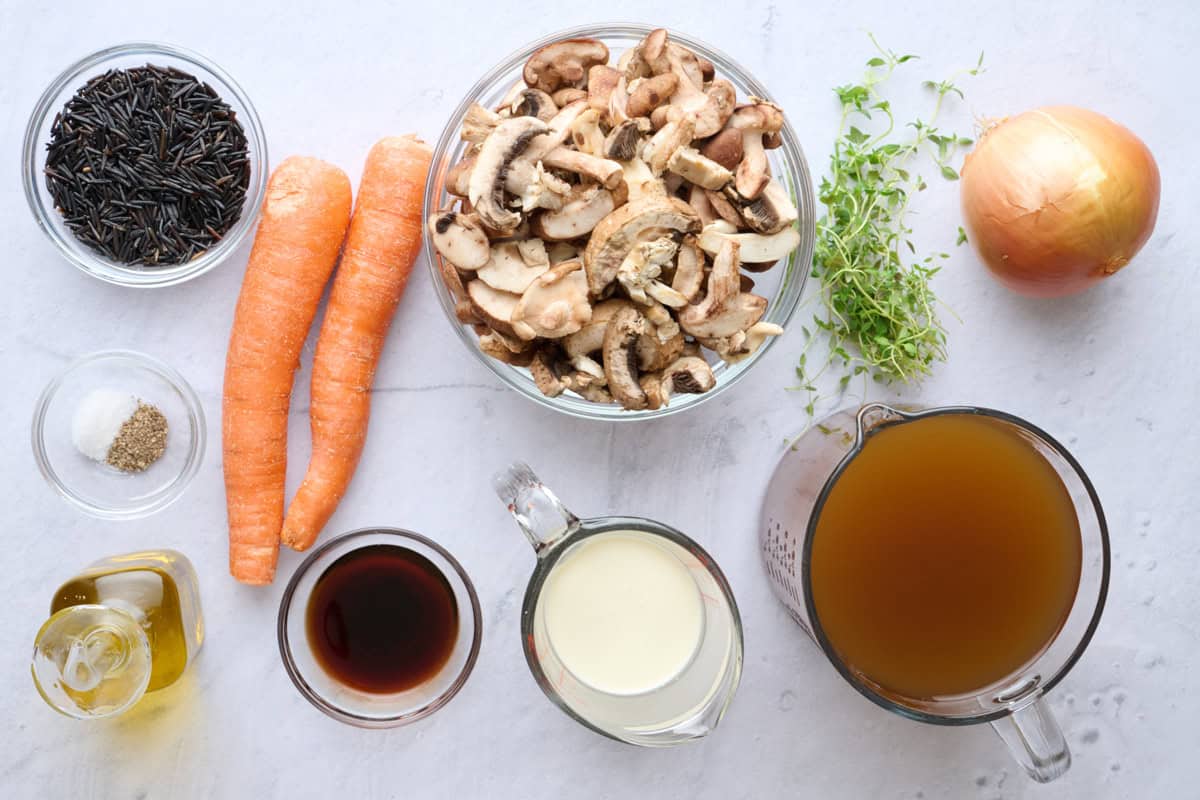 Ingredients for soup recipe: wild rice, 3 types of sliced mushrooms, carrots, salt and pepper, oil, balsamic vinegar, milk, broth, herbs, and onion.