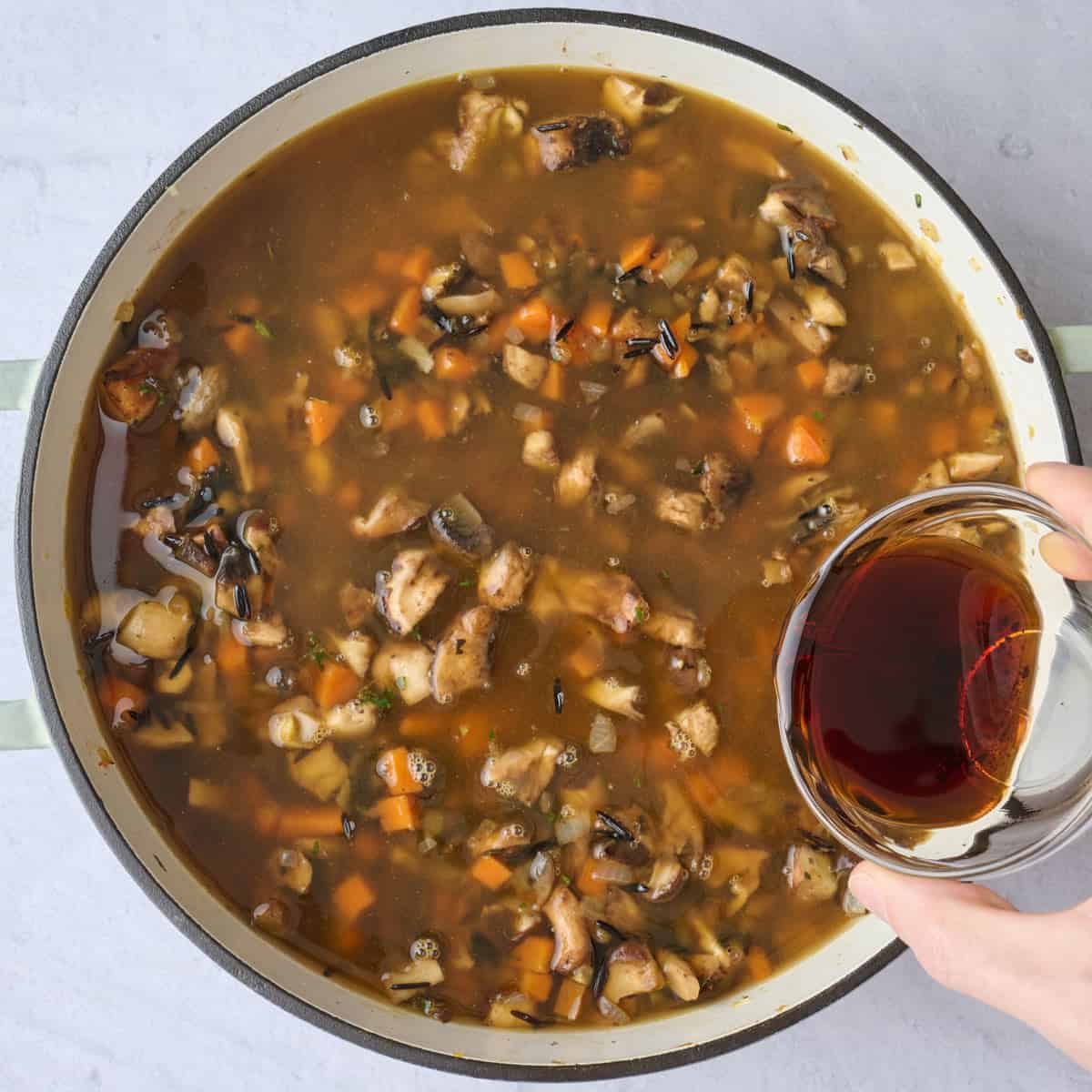 Broth added to mushroom and rice mixture in a pot with balsamic vinegar being poured in.