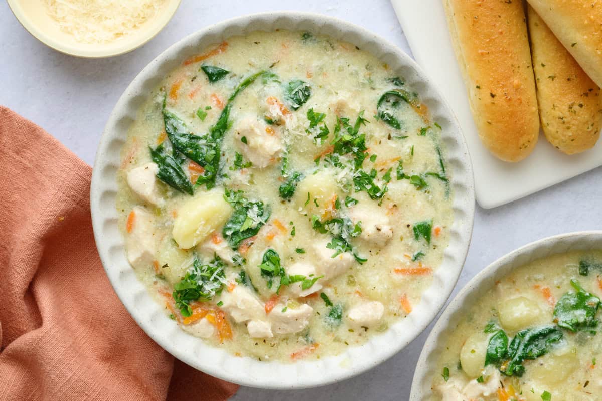 Easy chicken gnocchi soup in a bowl garnished with parmesan cheese and served with breadsticks.