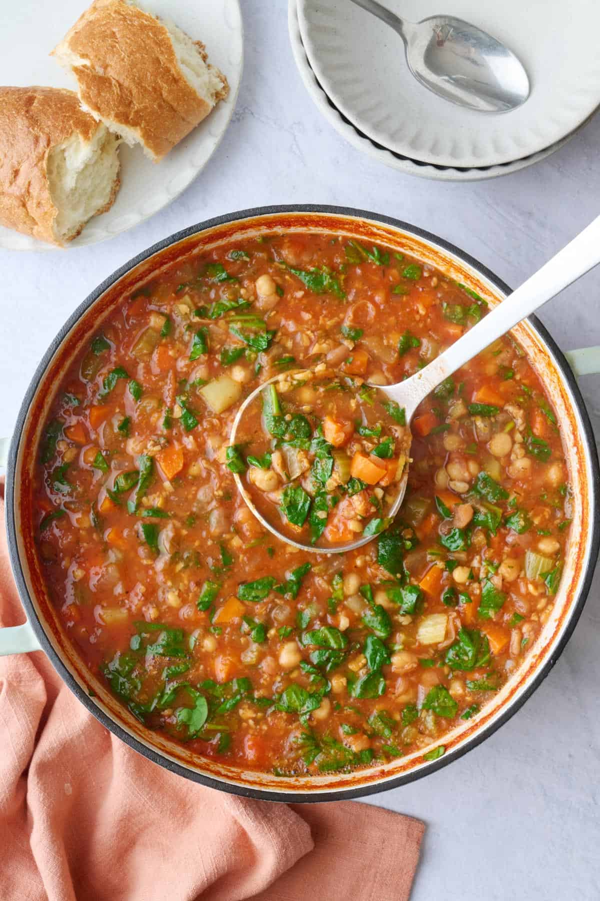 Chickpea soup with spinach in a pot with a ladle lifting some up.