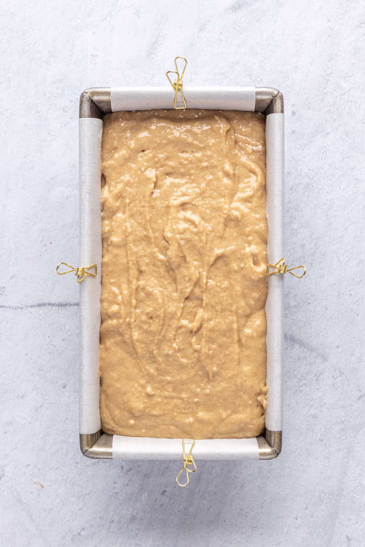Quick bread batter added to prepared loaf pan lined with parchment paper before baking.