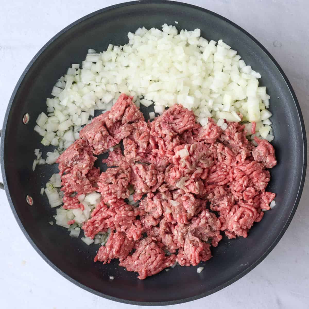 Ground beef and onions in a skillet after beef is broken up into pieces.