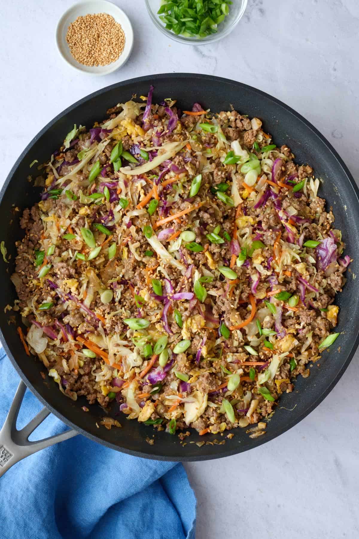 Best Egg roll in a bowl recipe in skillet with a small dish of green onions and sesame seeds nearby