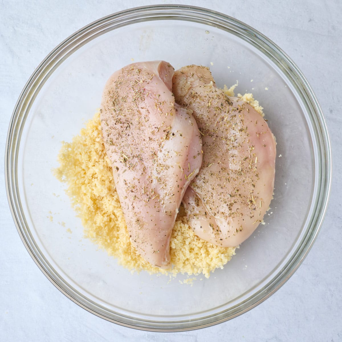 Parmesan breadcrumb mixture after tossing together with seasoned chicken breast on top before coating.