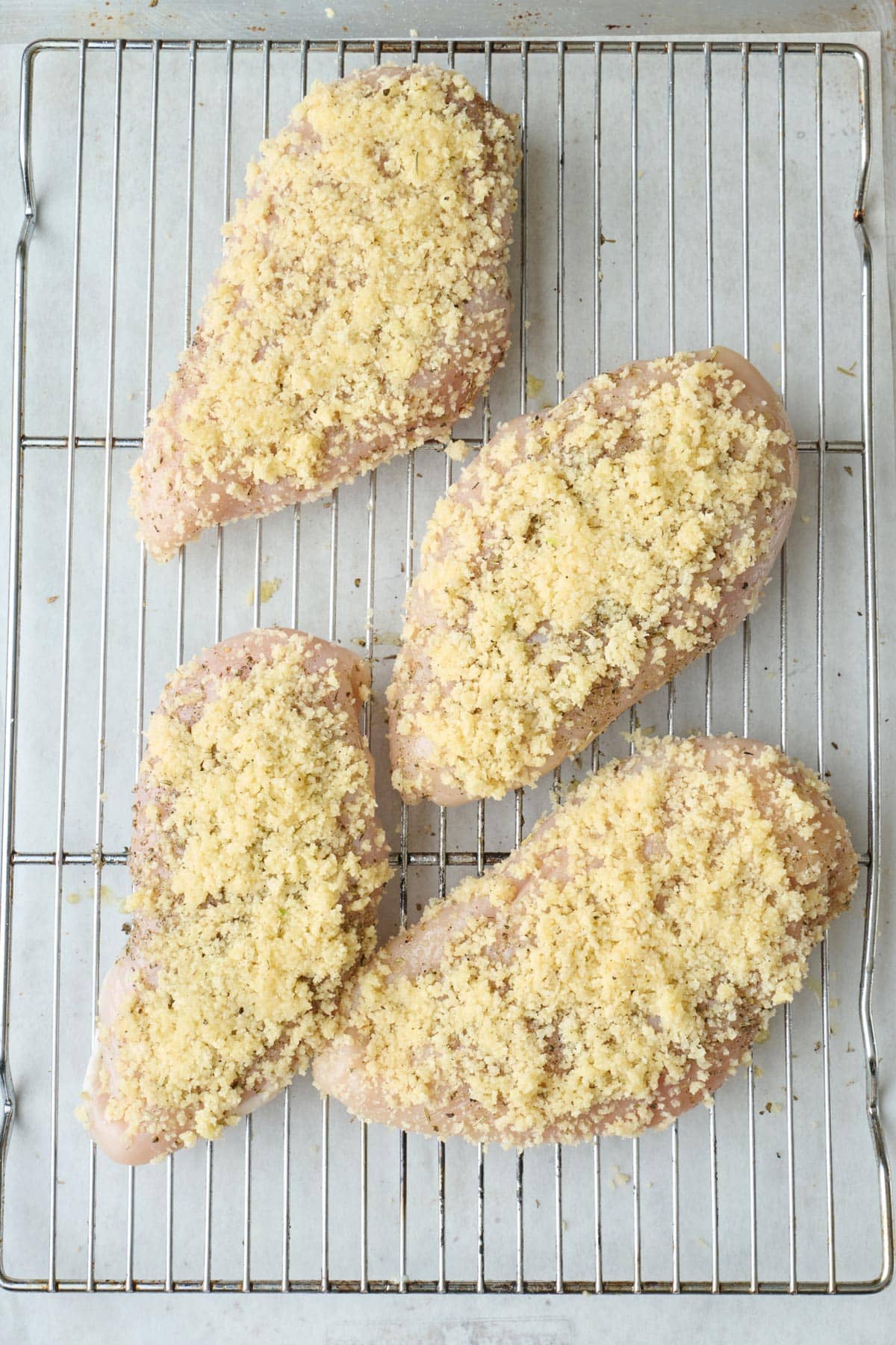 Parmesan panko coated chicken breasts on a wire rack on a prepared baking sheet before baking.