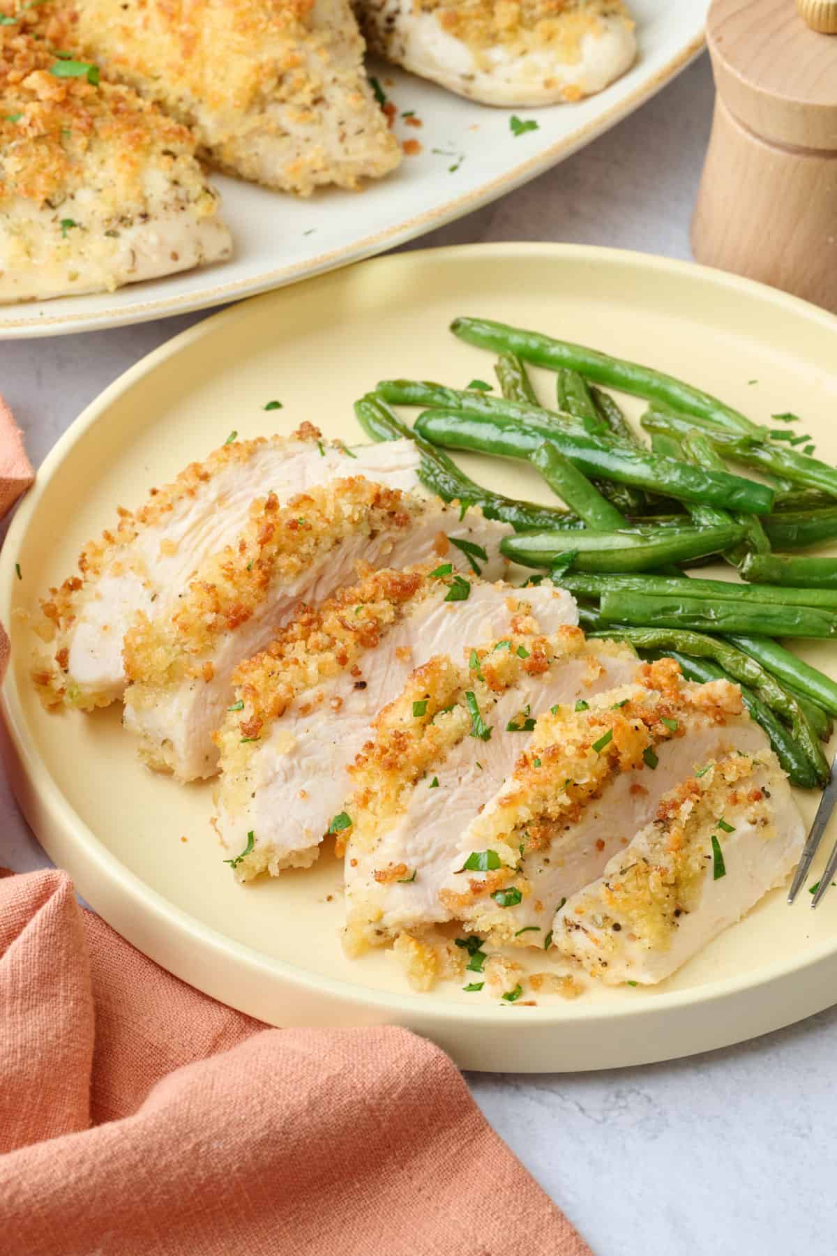 Sliced garlic parmesan chicken breast on a plate with green beans.