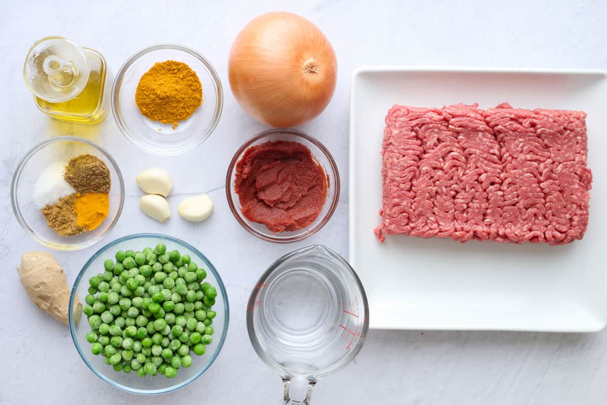 Ingredients for keema curry recipe: oil, seasonings, ginger, garlic, frozen peas, onion, tomato paste, water and ground beef.