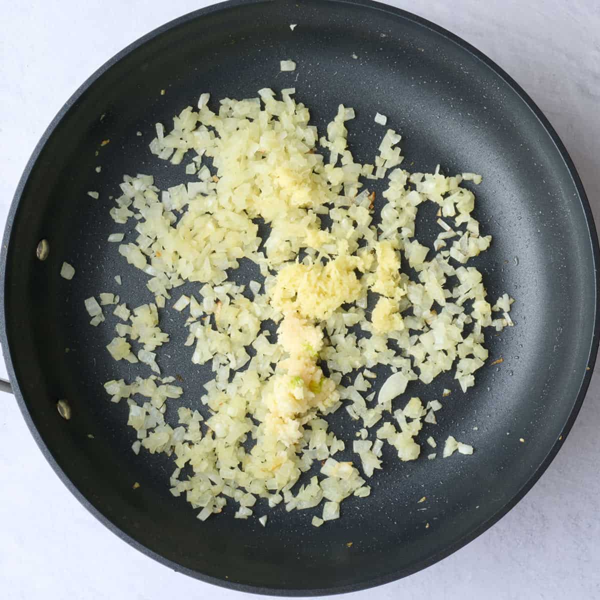 Cooked onions in a skillet with garlic and ginger added before stirring.