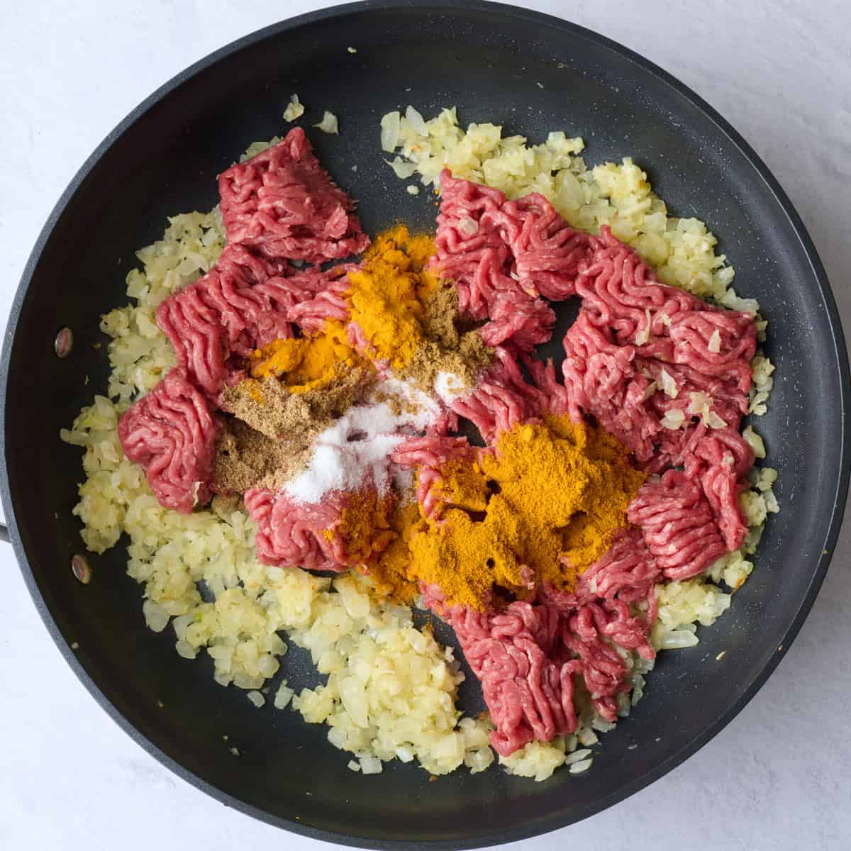 Ground beef, curry, salt, coriander, cumin, and turmeric added to cooked onions.