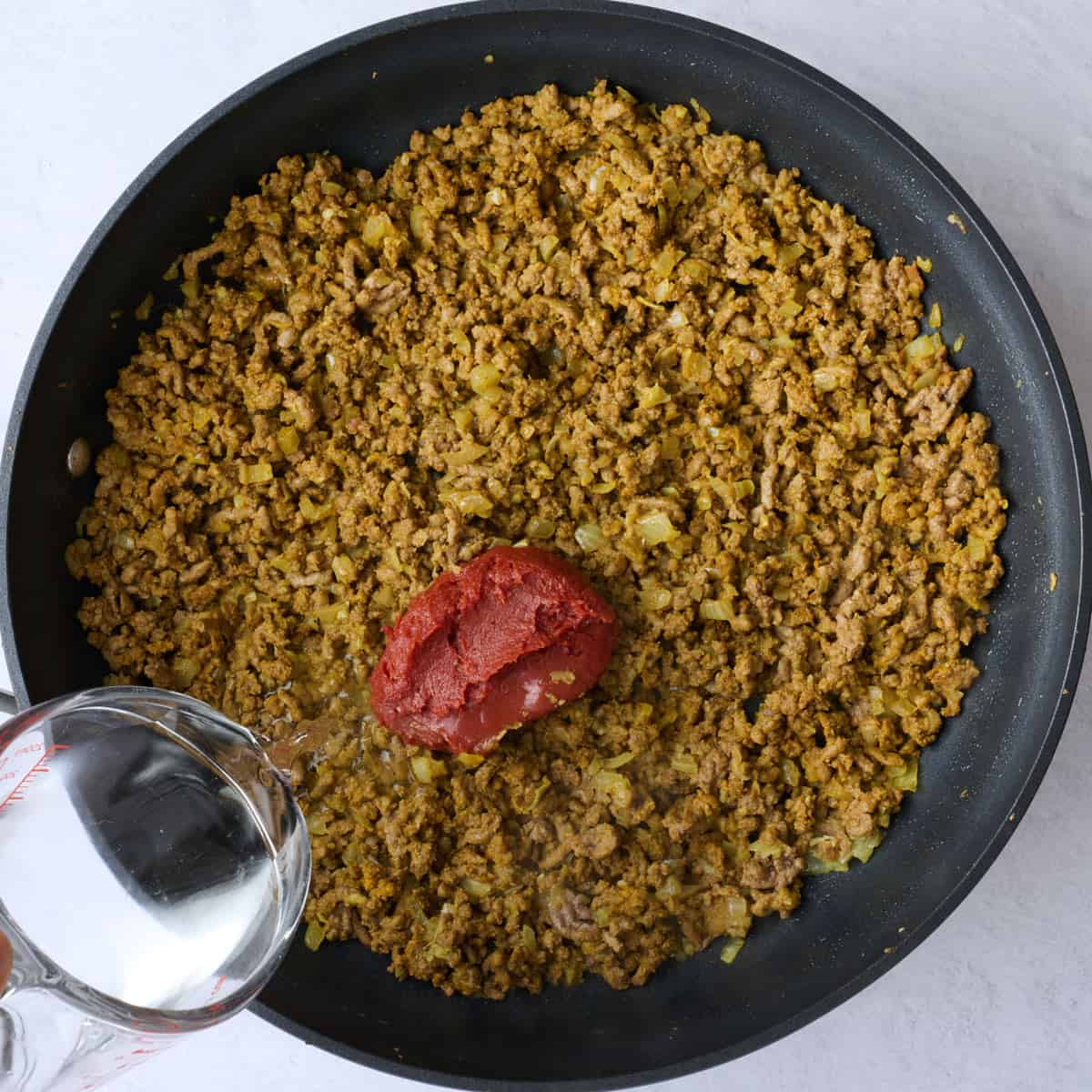 After ground beef is cooked and broken into pieces tossed with curry spices with tomato paste and water added.