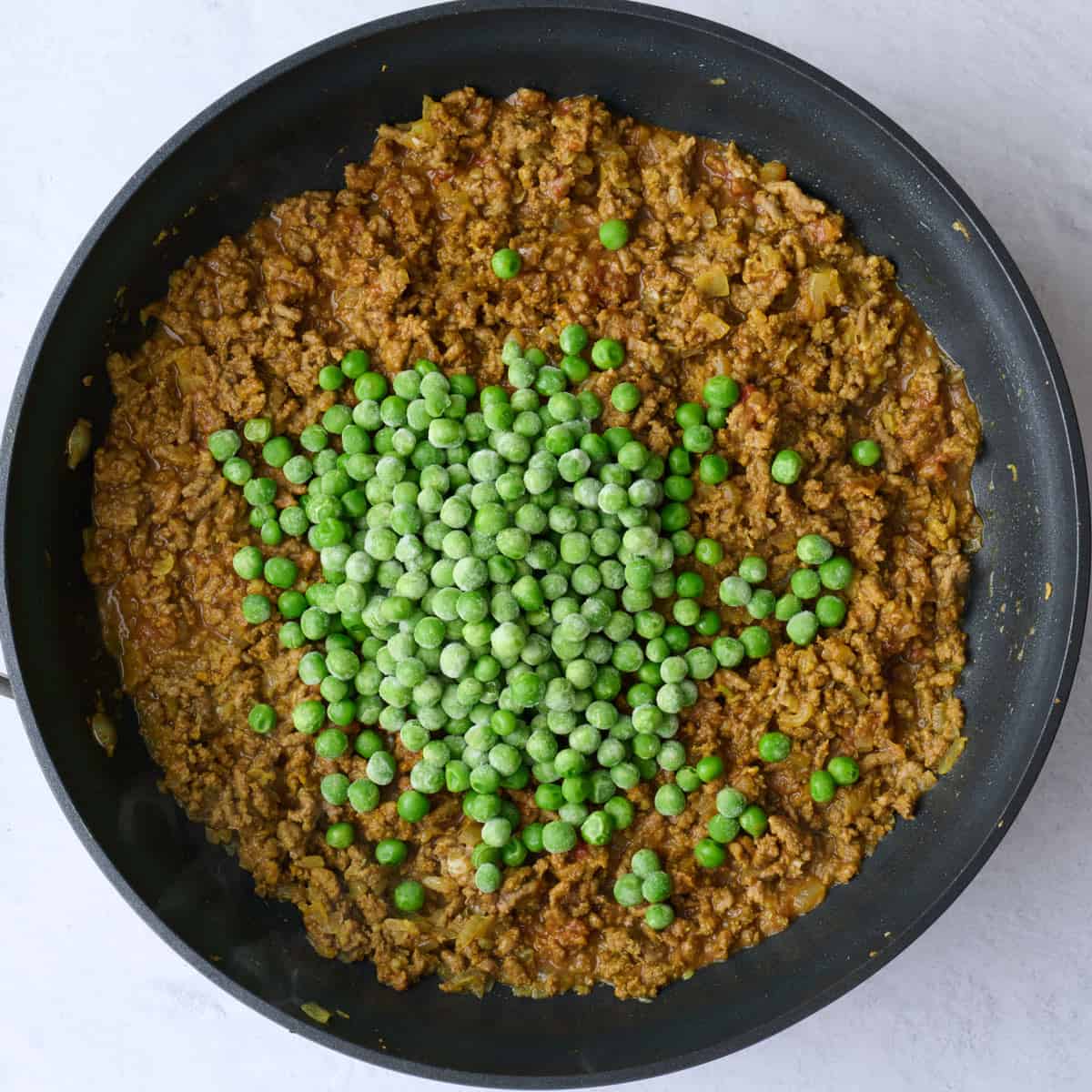 Frozen peas added on top of keema curry mixture.