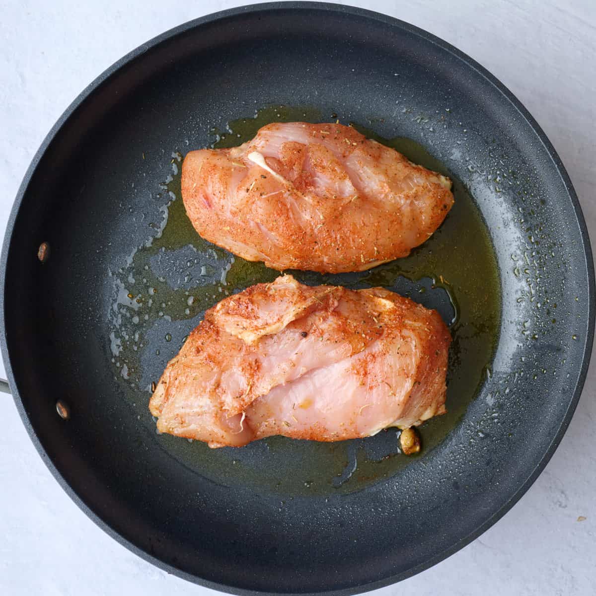 Seasoned chicken in an oiled skillet before cooking.