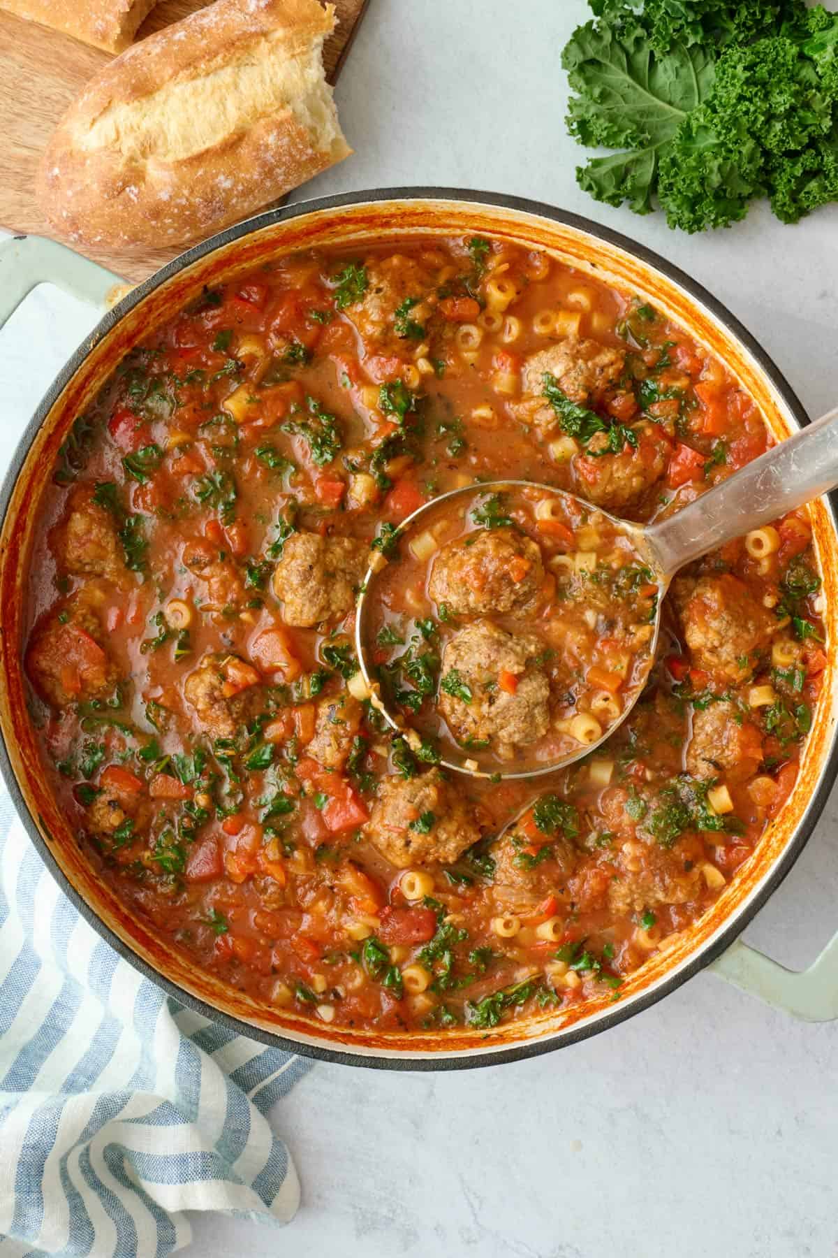 Meatball soup in the pot with a ladle lifting some up.
